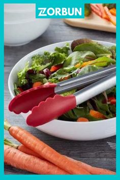 there is a salad in the bowl with utensils on it and two carrots next to it