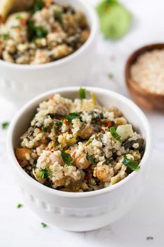 two bowls filled with rice and vegetables on top of a white table next to spoons