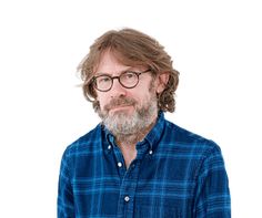 a man with glasses and a beard wearing a blue shirt is standing in front of a white background