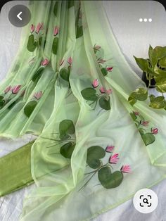 a green scarf with pink flowers on it next to a potted leafy plant