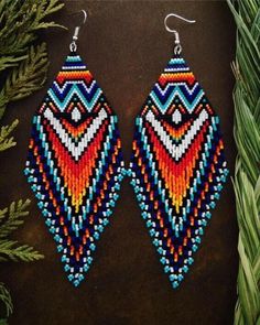 two pairs of beaded earrings with colorful designs on them, sitting next to some plants