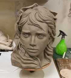 a clay sculpture of a woman's face on a table with a green sprayer