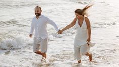 a man and woman holding hands walking into the ocean