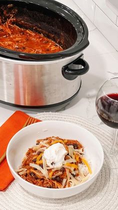 a bowl of food next to a glass of wine on a white tablecloth with an orange napkin