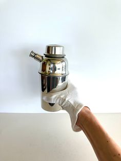 a person's hand holding a silver coffee pot with a white glove on it