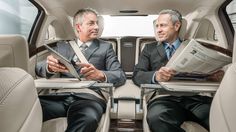 two men sitting in the back of a car holding papers and looking at each other