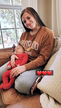 a woman sitting on a couch holding a baby in her lap and smiling at the camera