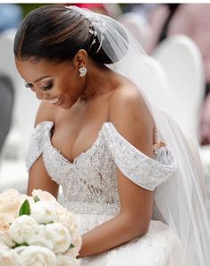 a woman in a wedding dress is looking down at her bouquet while sitting on a chair