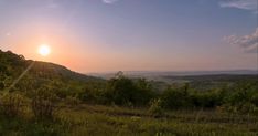 the sun is setting over some hills and trees