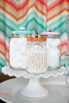 three glass jars filled with white cotton sitting on top of a cake plate next to other items