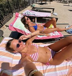 two women in bikinis laying on towels at the beach