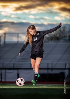 a woman kicking a soccer ball on top of a green field with the sky in the background