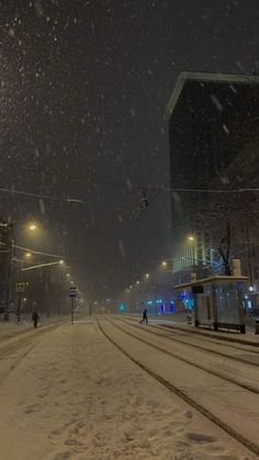 a snowy street at night with people walking on the sidewalk and buildings in the background