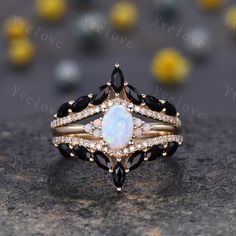 a white opal and black diamond ring set on top of a stone surface with yellow flowers in the background