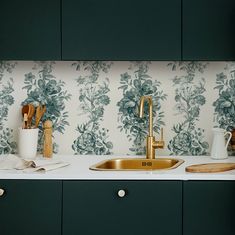 a kitchen with green and white wallpaper, gold faucet sink and wooden utensils