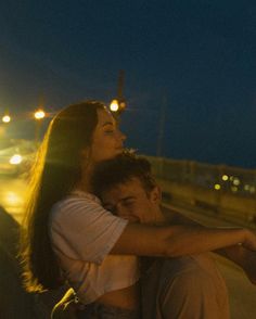 a man hugging a woman on the side of a road at night with street lights in the background