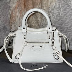 Nwt Balenciaga Neo Classic Crocodile-Embossed Leather City Bag In Rare And Hard To Find Croc-Embossed White With Silver-Tone Hardware. Versatile And Can Be Worn In Different Ways: Shoulder Bag, Crossbody Or As A Top Handle Bag. Balenciaga Logo In Front With Buckle Accents Exterior Pocket Zippered Top Closure Double Top Handles With 4” Drop Removable And Adjustable Crossbody/Shoulder Strap With 20” Drop Leather Lined With One Interior Pocket Comes With Dust Bag And Tags But Unfortunately No Authe Luxury White Bag With Crocodile Pattern, Balenciaga Neo Classic Mini, Balenciaga Neo Classic, Balenciaga Logo, Neo Classic, Balenciaga Bag, City Bag, Classic Mini, Handle Bag