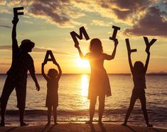 silhouettes of people holding up letters on the beach at sunset with the sun setting in the background