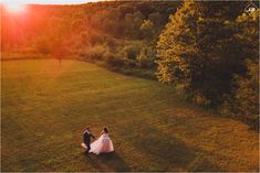 a bride and groom walking in the grass at sunset