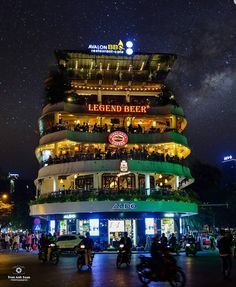 the building is lit up at night with many people on bikes and scooters