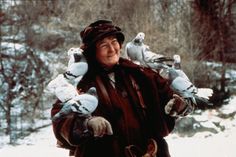 an older woman holding two birds in her hands while standing on the snow covered ground