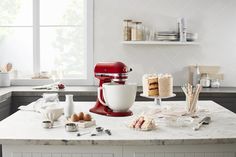 a red mixer sitting on top of a kitchen counter next to cakes and other items