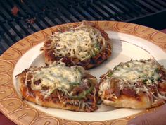 three small pizzas on a plate being held by someone's hand over an outdoor grill