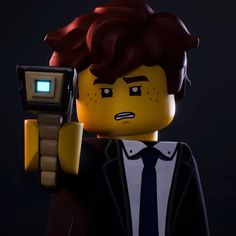 a lego man holding a cell phone up to his face in front of a dark background