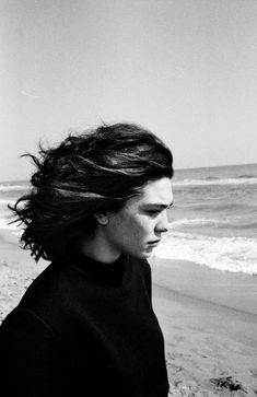 a woman walking on the beach with her hair blowing in the wind, black and white photograph