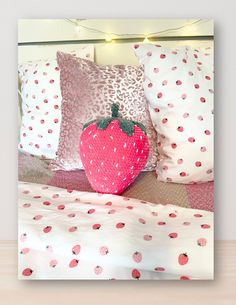 a strawberry pillow sitting on top of a bed covered in white and pink polka dots