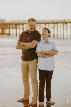 two men standing next to each other in the water at the beach with a pier in the background