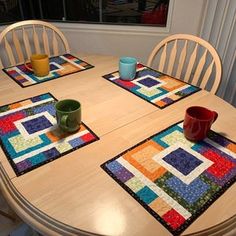 a wooden table with four place mats on top of it and two mugs at the end