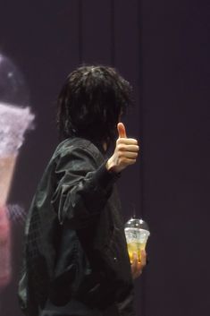 a man giving a thumbs up while holding a drink in front of a large screen