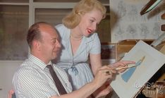 a man and woman are looking at something on a easel while the woman is drawing