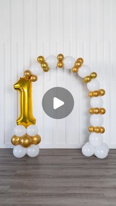 an arch made out of balloons with the number one balloon in gold and white colors