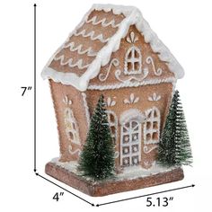 a gingerbread house ornament is shown with pine trees and snow on the roof