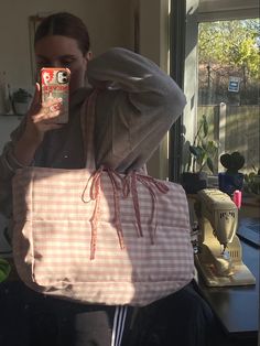 a woman taking a selfie while holding a pink and white tote bag in front of her face