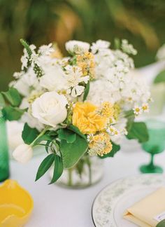 a vase filled with white and yellow flowers sitting on top of a table next to plates