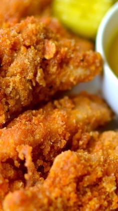 some fried food on a white plate with pickles and breadcrumbs in the background