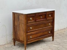 an old wooden dresser with marble top sitting on the ground next to a white wall