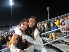 two young women hugging each other in front of an empty bleachers at night