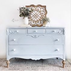 a white dresser sitting on top of a carpeted floor next to a vase filled with flowers