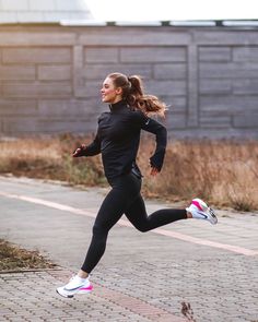 a woman is running down the street in a black jacket and leggings with pink accents