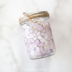 a jar filled with purple and white flowers on top of a marble counter next to a string