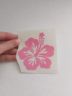 a hand holding a pink and white sticker with a flower on it's side