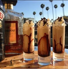 three glasses filled with ice cream and chocolate on top of a table next to a bottle