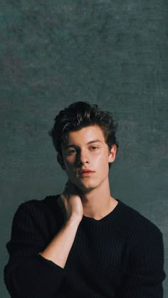 a young man is posing for the camera with his hand on his chin and wearing a black sweater