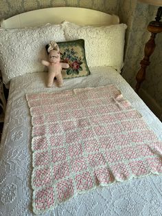 a small teddy bear sitting on top of a bed next to a pillow and blanket