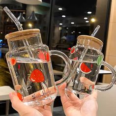 two people holding up clear mugs with strawberries on the inside and one is filled with water