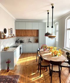 a kitchen and dining room with hardwood floors, white cabinets and wooden table surrounded by chairs